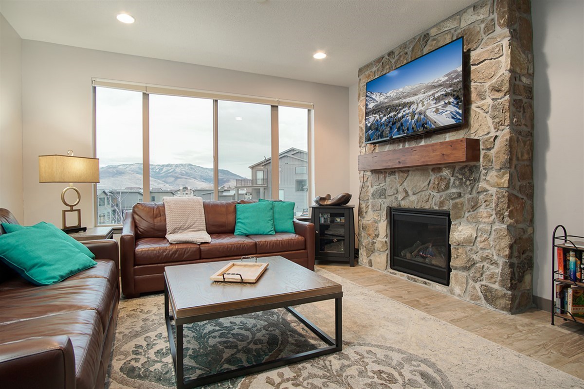 A refined main-level living room anchored by a stunning stone fireplace, where expansive windows frame sweeping mountain views and elevate every moment of relaxation.