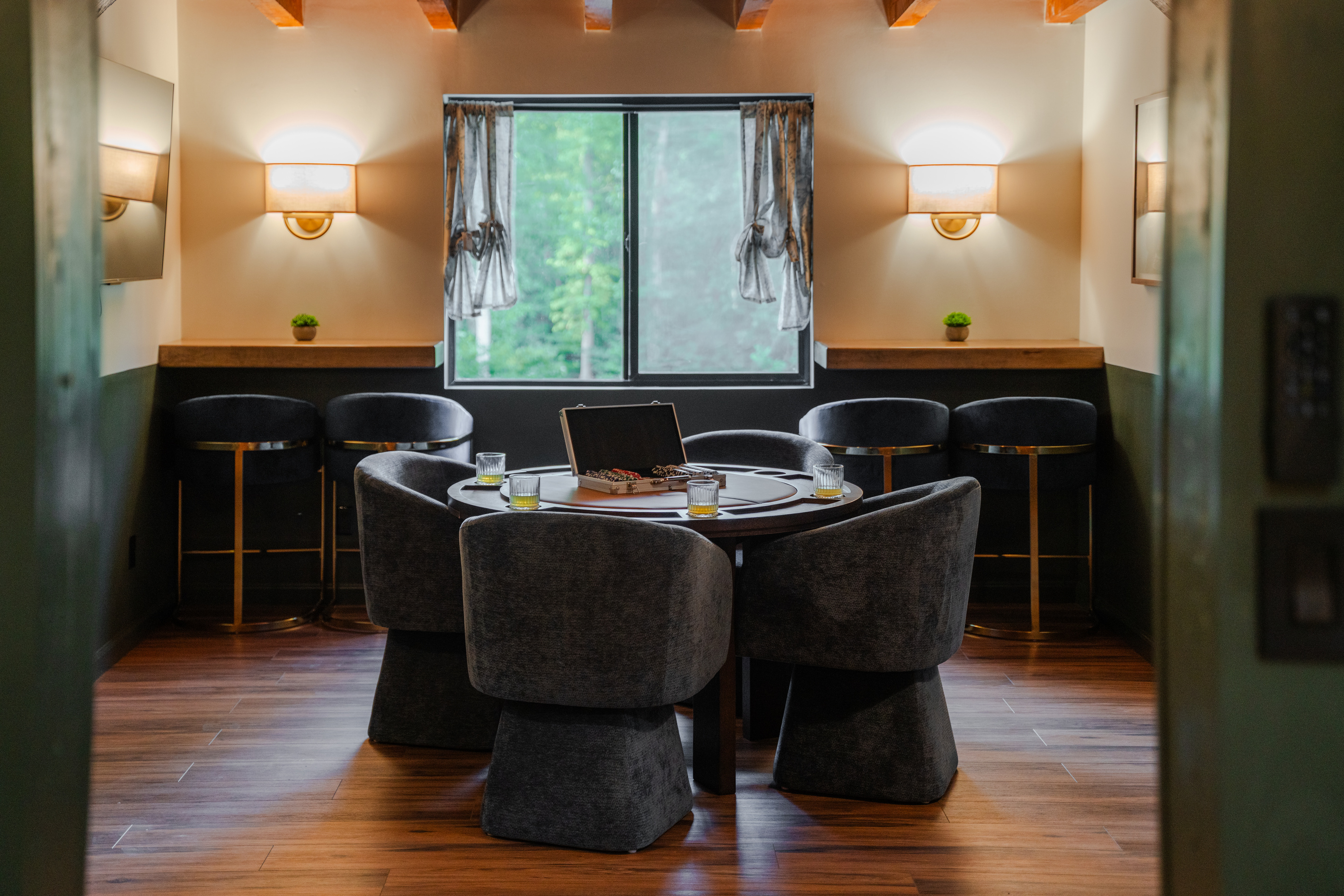 Open family lounge featuring a TV, poker/game table, bar seating, and peaceful wooded views