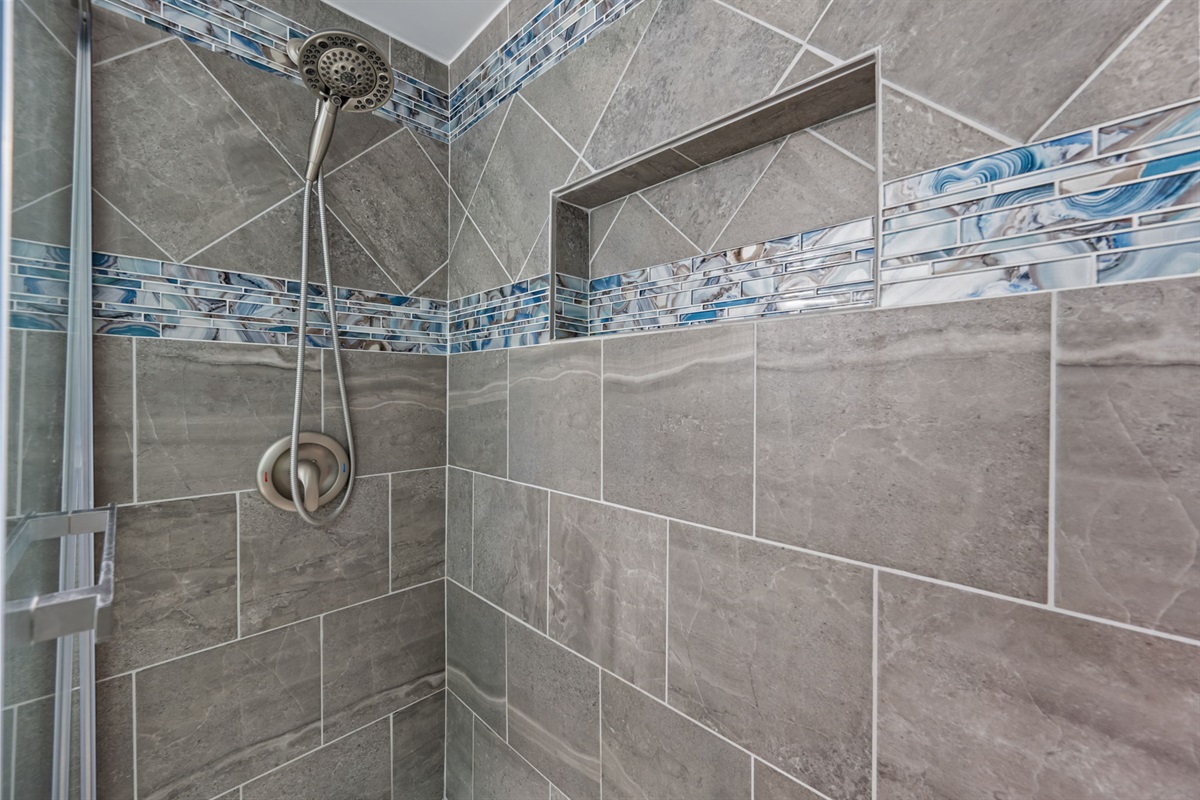 Spacious walk-in shower with custom tilework, built-in niche, and handheld showerhead for added comfort