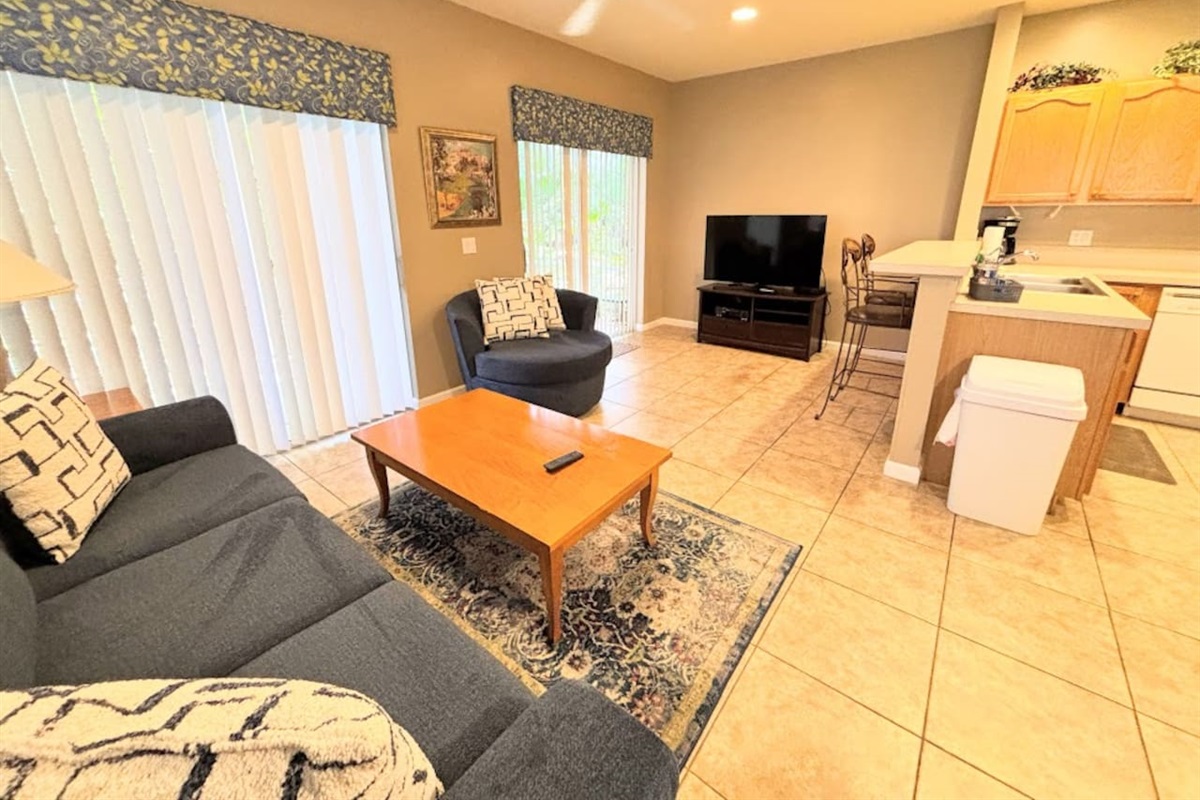 Comfortable open living area with tile flooring, cozy seating, large TV, and sliding glass doors bringing in natural light.