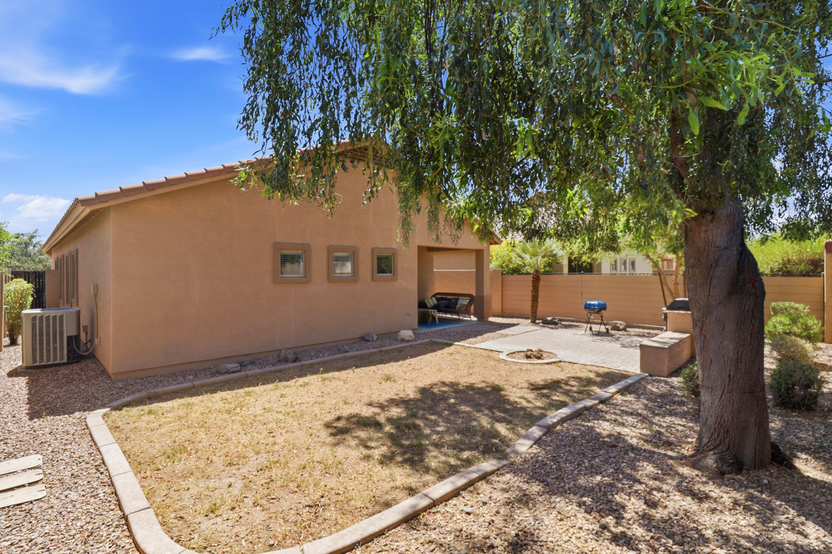 Fenced backyard with shade from the tree, a BBQ grill, and space to spend time outside.
