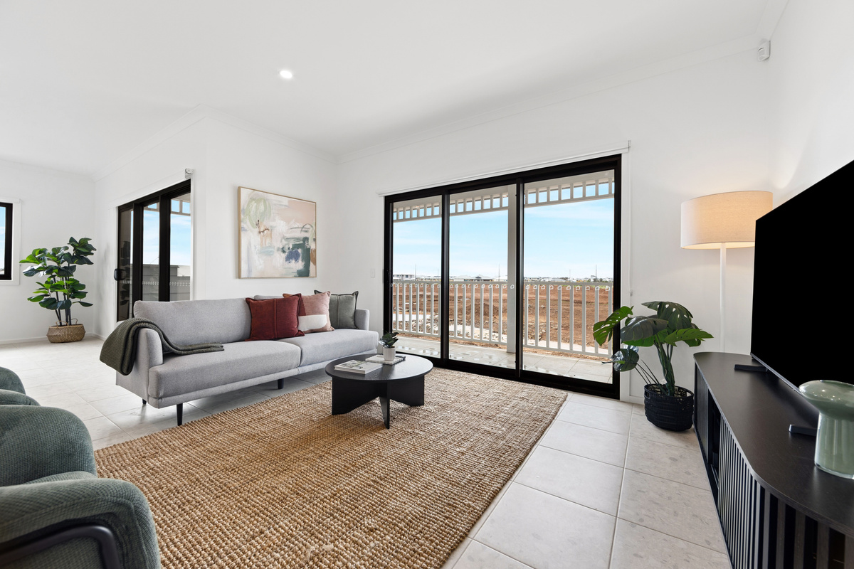 Lounge with a large TV, grey sofa and green armchairs on a jute rug, with sliding doors opening to the balcony.
