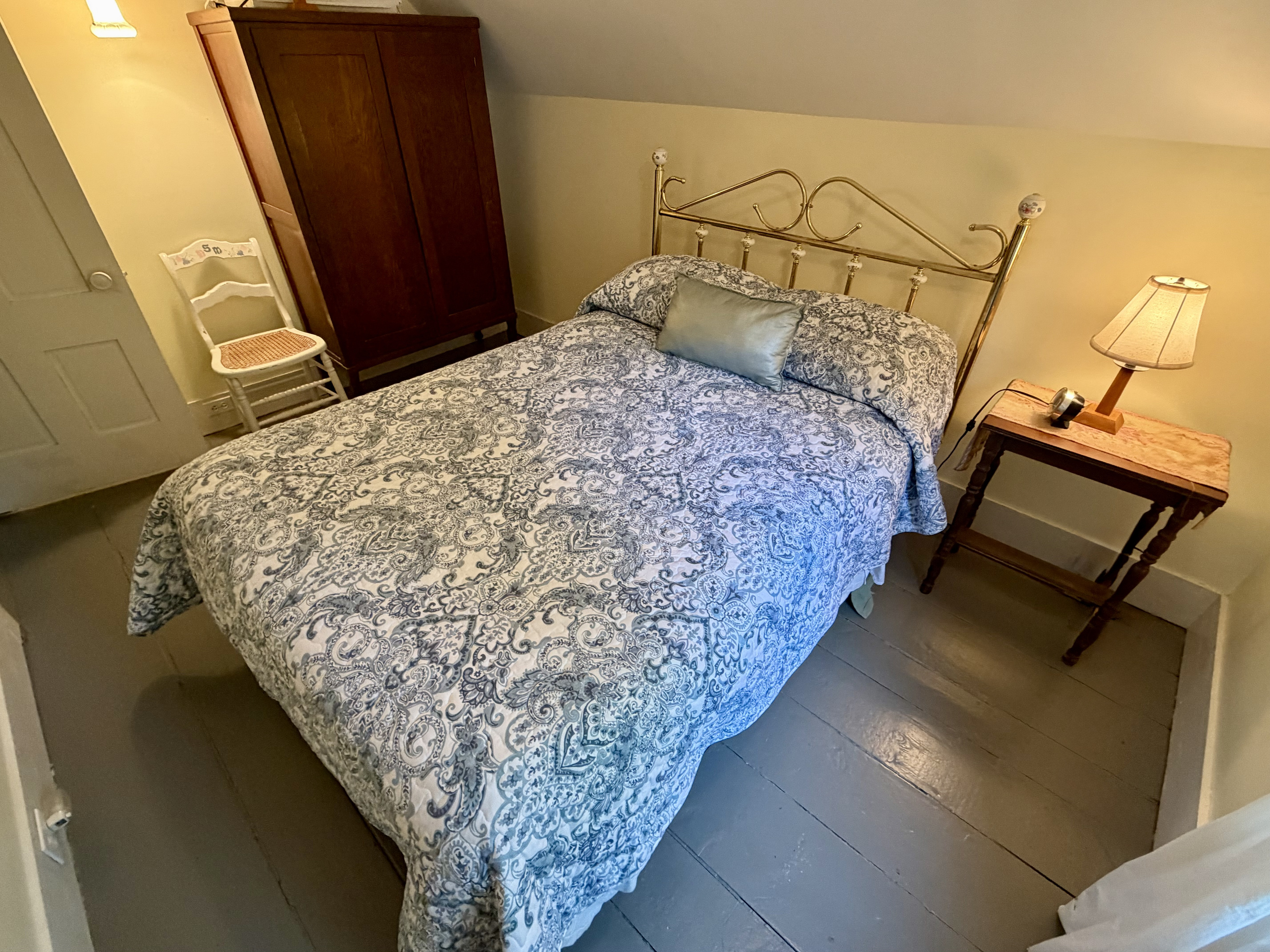 The guest bedroom features a handsome antique wardrobe, offering ample storage space for your belongings. This cozy room beautifully pairs original charm with functional modern comfort for a restful stay near Acadia.