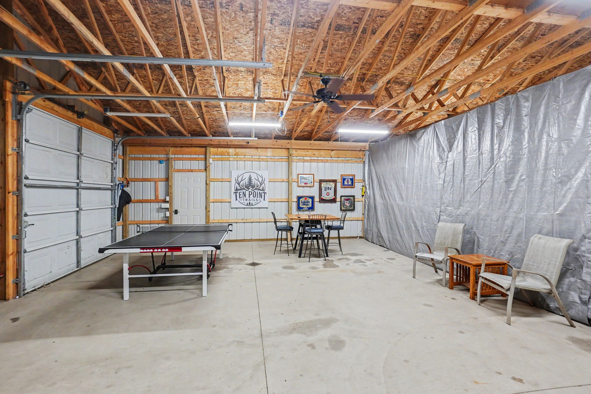 Garage game room with ping pong table, darts, tv and table and chairs.