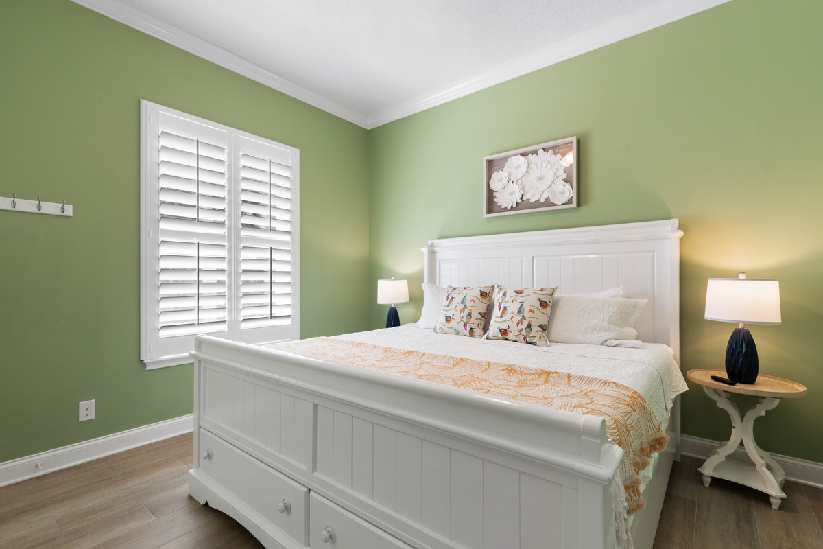 Green Suite with a white cottage-style king bed, coral linens and bird-print pillows for a calm, restful stay.