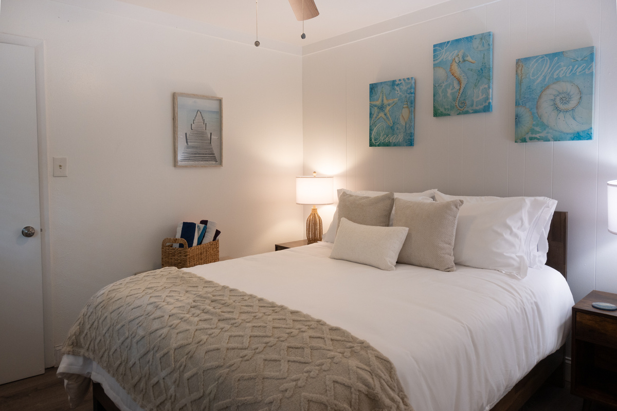 Queen bed with crisp hotel-quality linens and soft coastal art