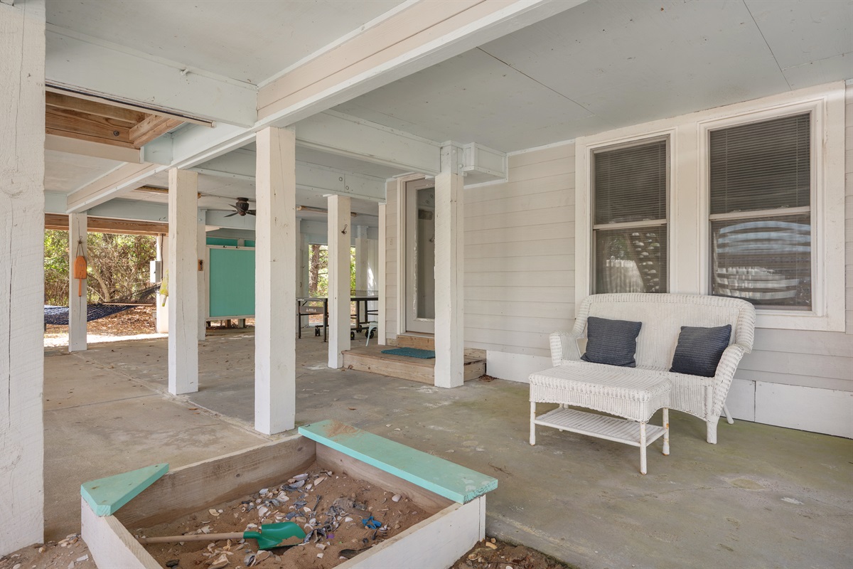 Covered outdoor lounge space with shaded seating and a kids’ sandbox for extra family fun.