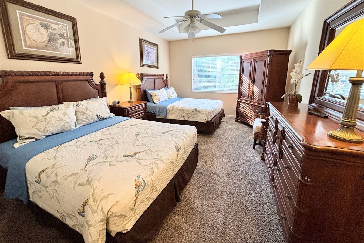 Spacious bedroom featuring two comfortable beds, ceiling fan, ample dresser storage, and warm natural light for a relaxing stay.