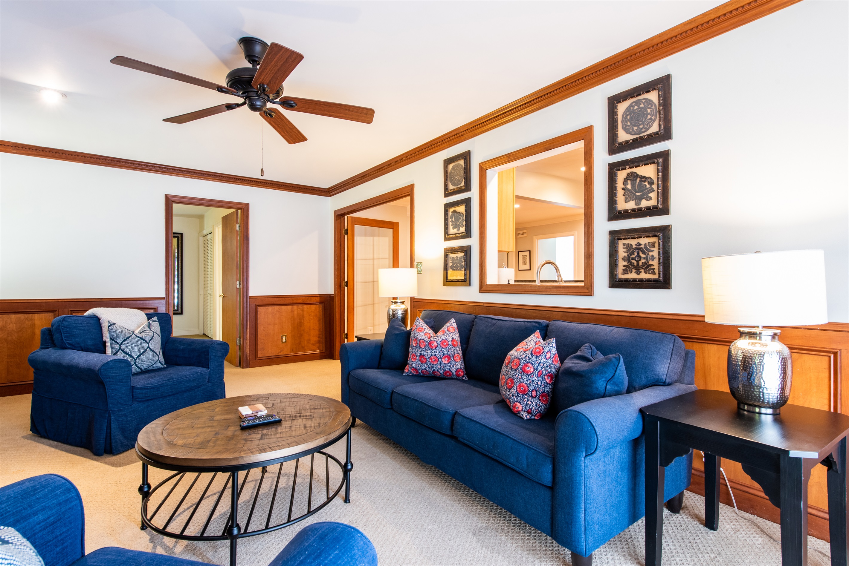 nviting Airbnb in Louisville, KY, on the Bourbon Trail. Spacious living room with blue sofa, armchair, red pillows, wooden coffee table, lamps, and framed art. Ideal for a cozy retreat.