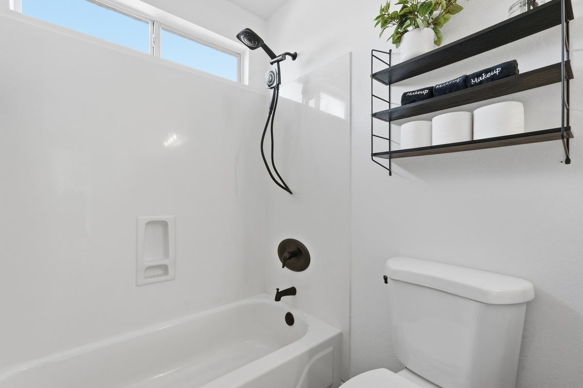 Full Bathroom 2 with a shower/tub combination, handheld showerhead, and wall shelf stocked with extra bath essentials.