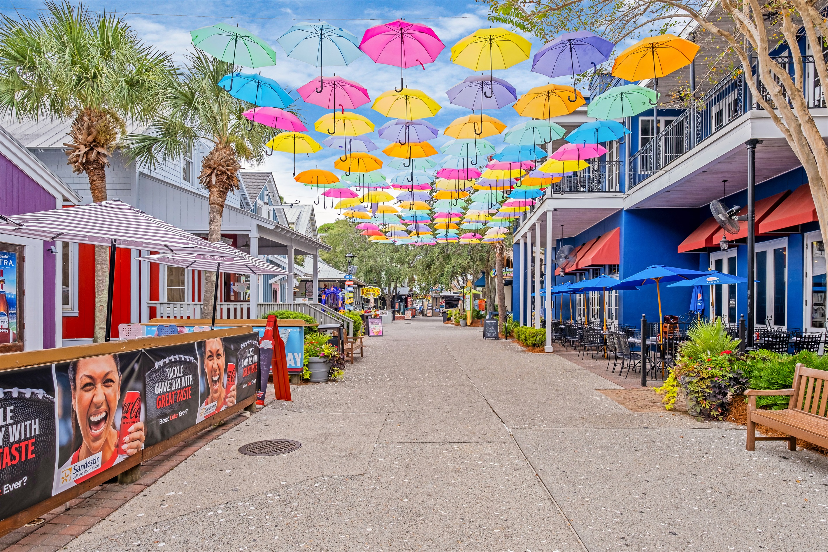 Vibrant umbrellas line the sky above this charming walkway, inviting visitors to enjoy the festive atmosphere of the town square.