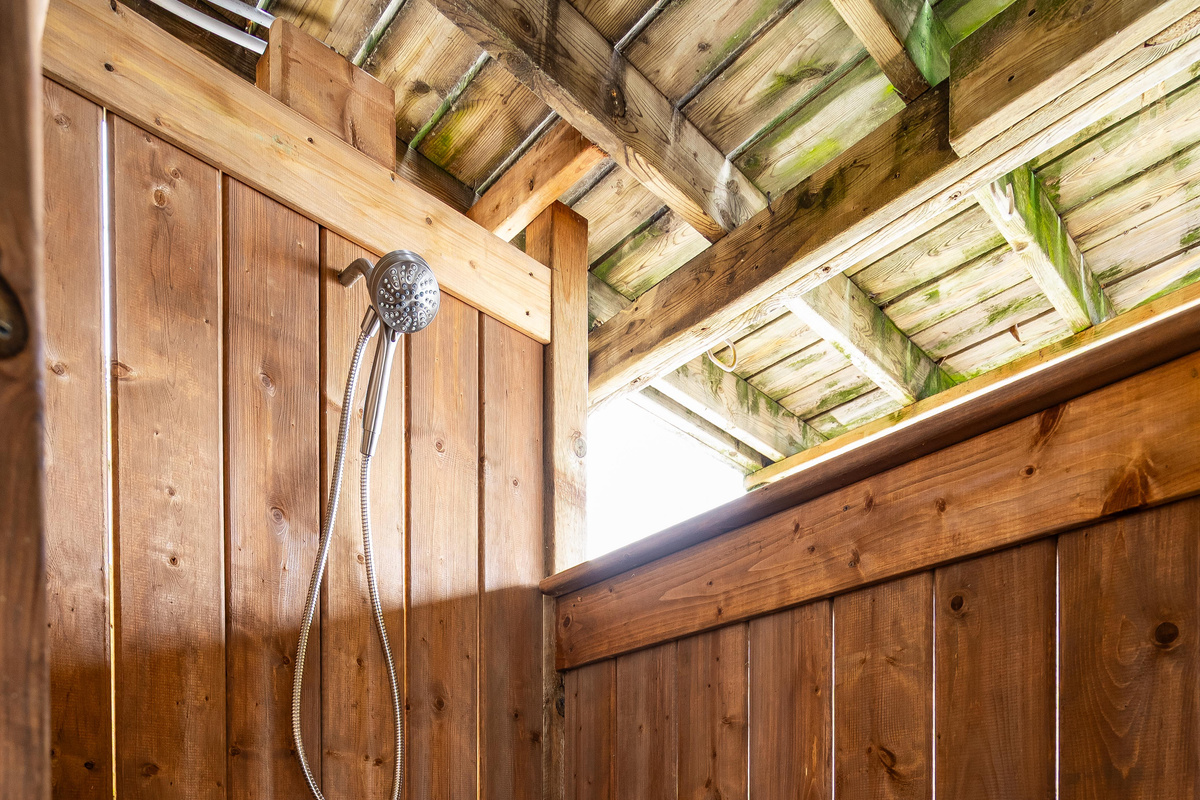 Charming wood-paneled outdoor shower with exposed timber ceiling and natural light.