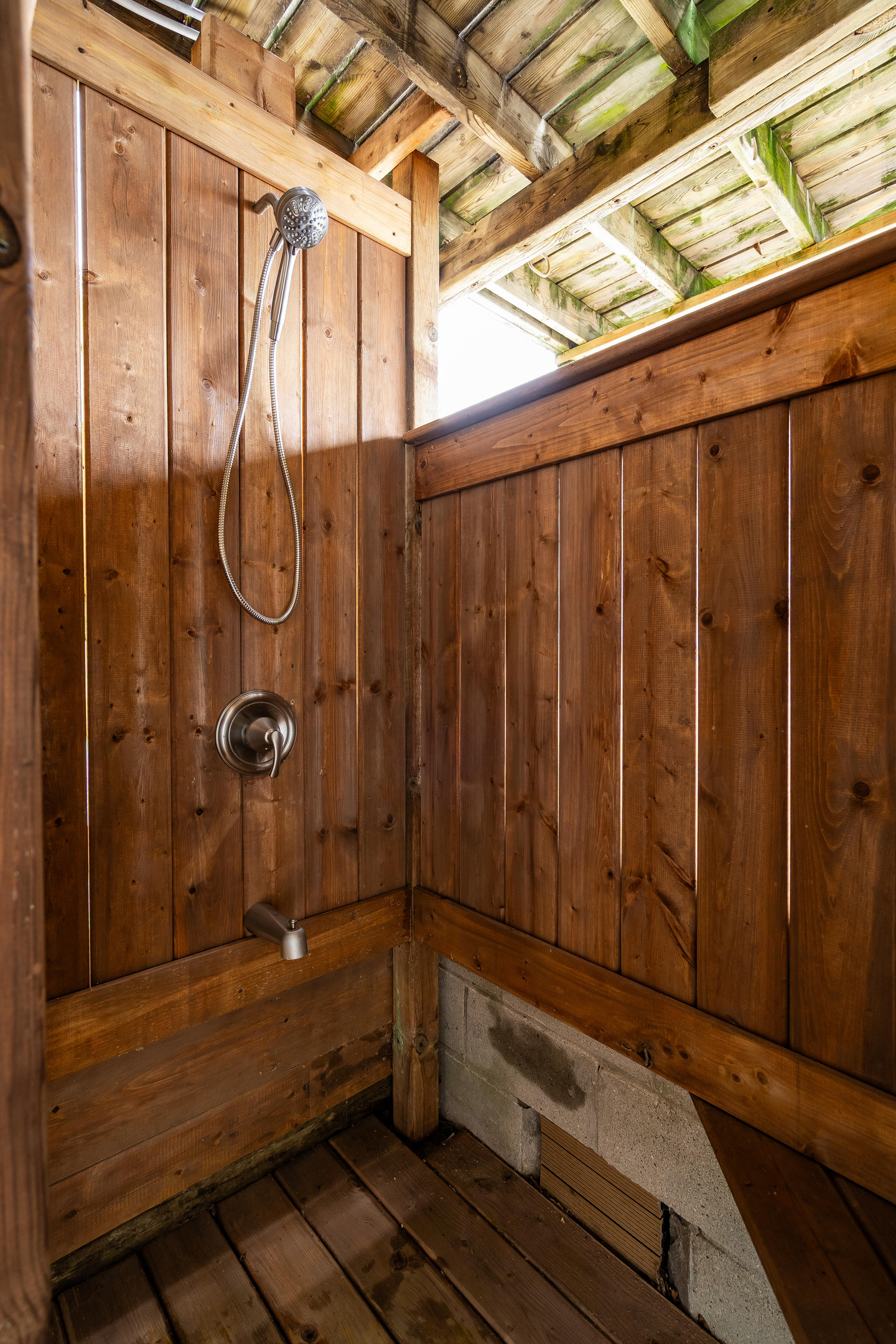 Charming wood-paneled outdoor shower with exposed timber ceiling and natural light.