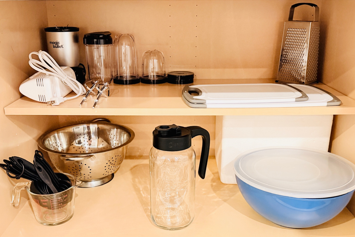 Kitchen cabinet stocked with cookware, mixing bowls, and food-preparation essentials.