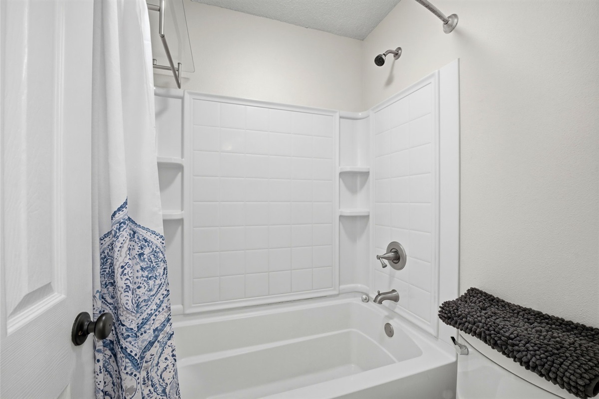 This clean and spacious bathroom features a full tub and shower combination, perfect for relaxing after a day at the beach. Built-in shelving provides convenient storage, while bright finishes keep the space fresh and inviting.