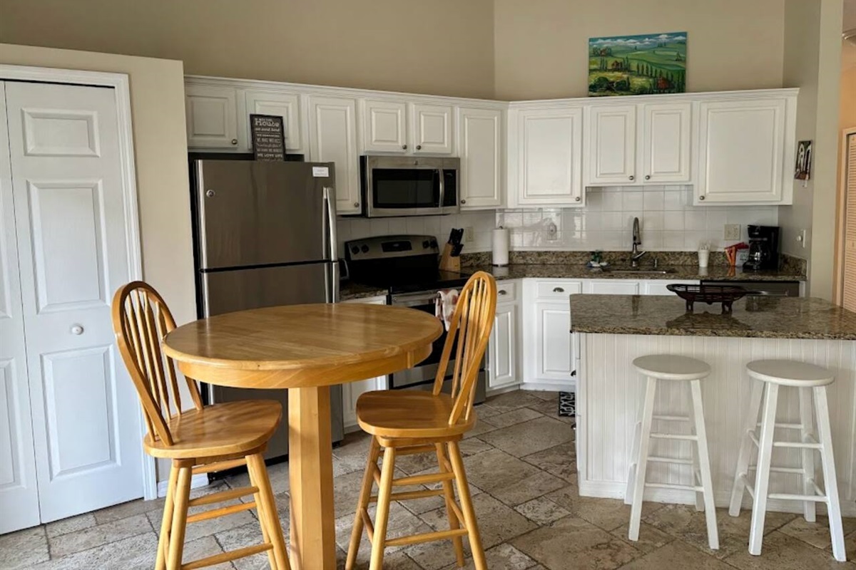 Open kitchen and dining area featuring white cabinetry, granite countertops, breakfast bar seating, and a round dining table.