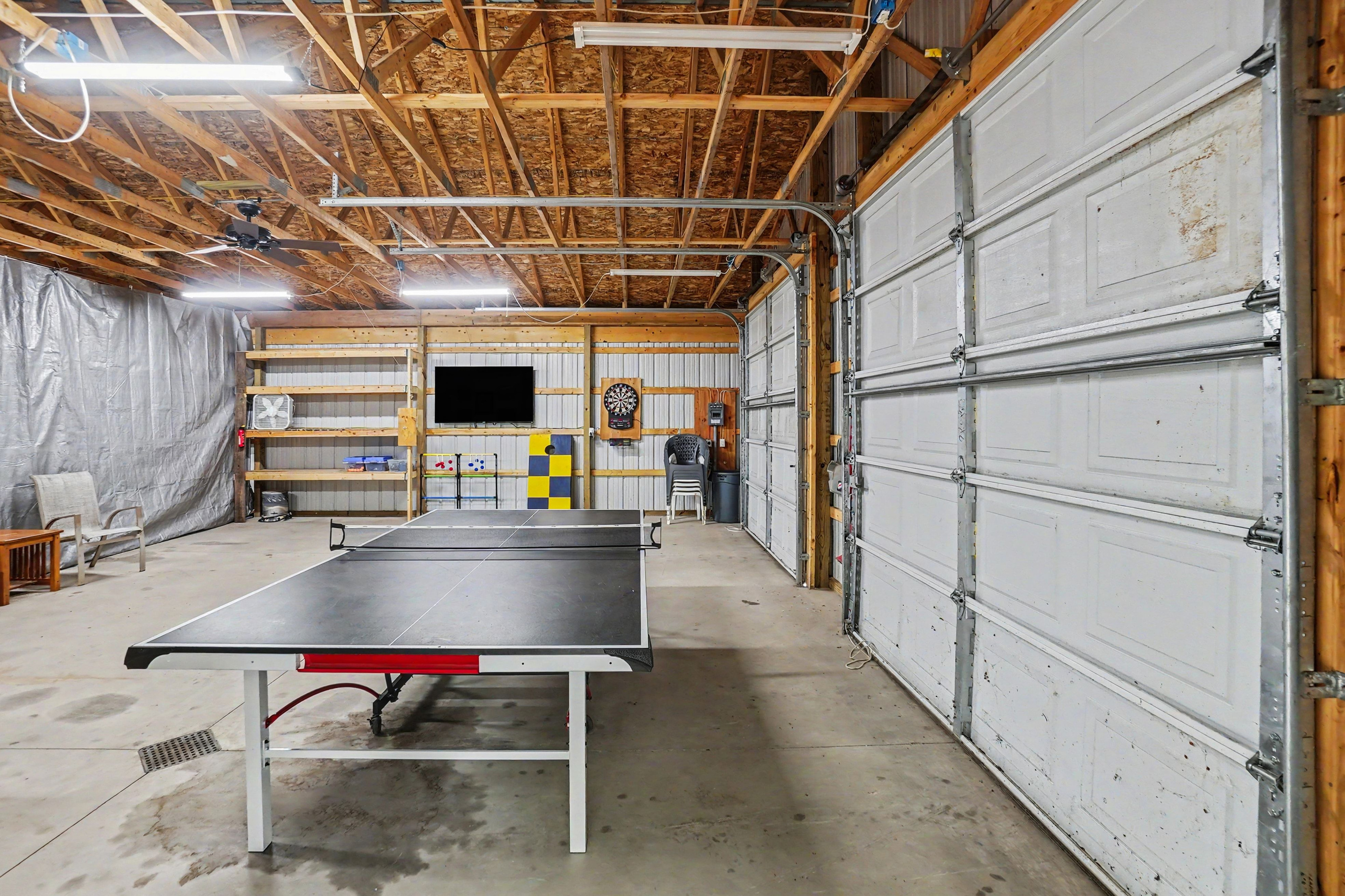 Garage game room with ping pong table, darts, tv and table and chairs.