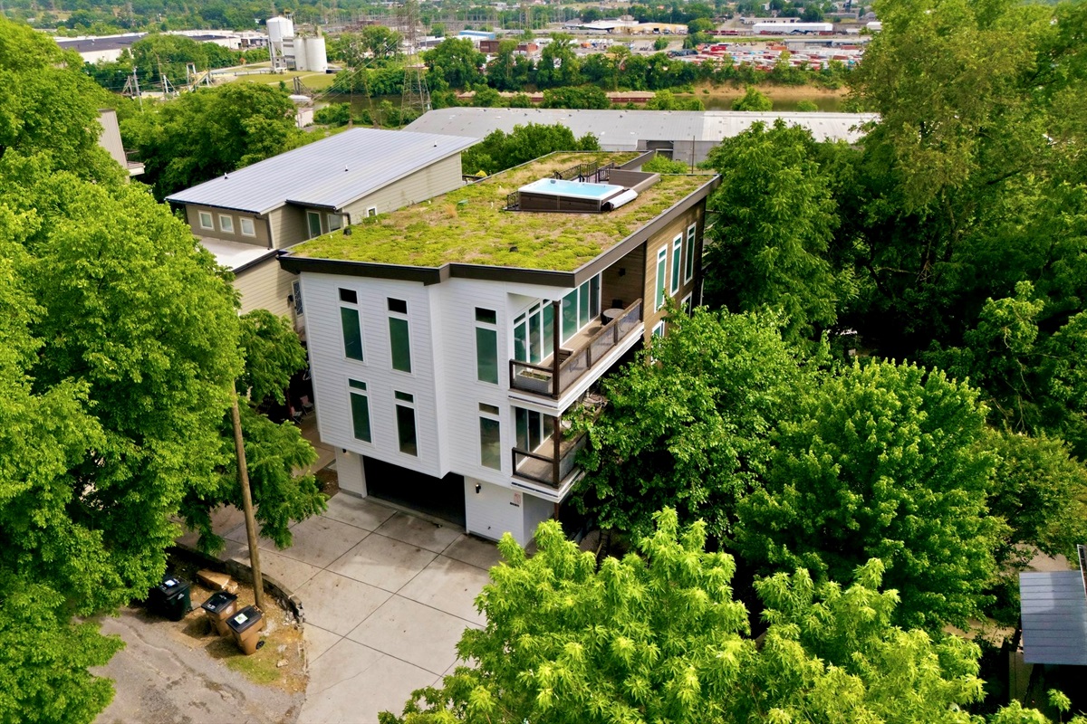 Aerial view of the full property w/ a living green roof & tree-lined surroundings.
