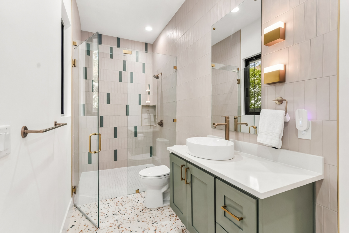 Green mosaic tile and a vessel sink vanity add character to this bathroom.