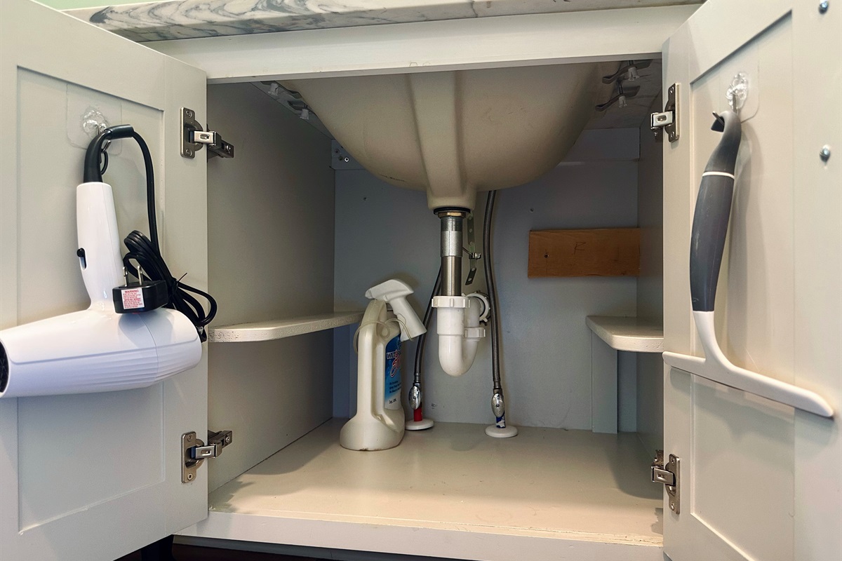Right-side ensuite cabinet featuring a hair dryer and shower cleaning supplies, thoughtfully provided for guest convenience.