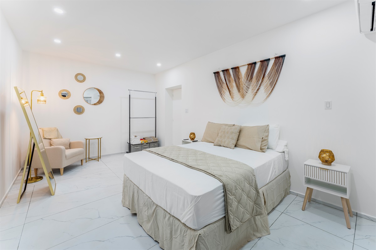 Ground floor bedroom: Wide shot of beige/gold bed with reading chair and mirror