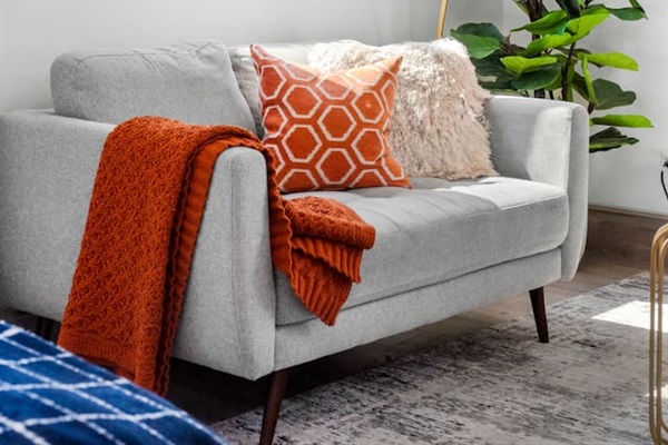 This living room radiates warmth and thoughtful design! The combination of the cozy gray sofa, textured pillows, and that inviting orange blanket creates a perfect space for relaxation.