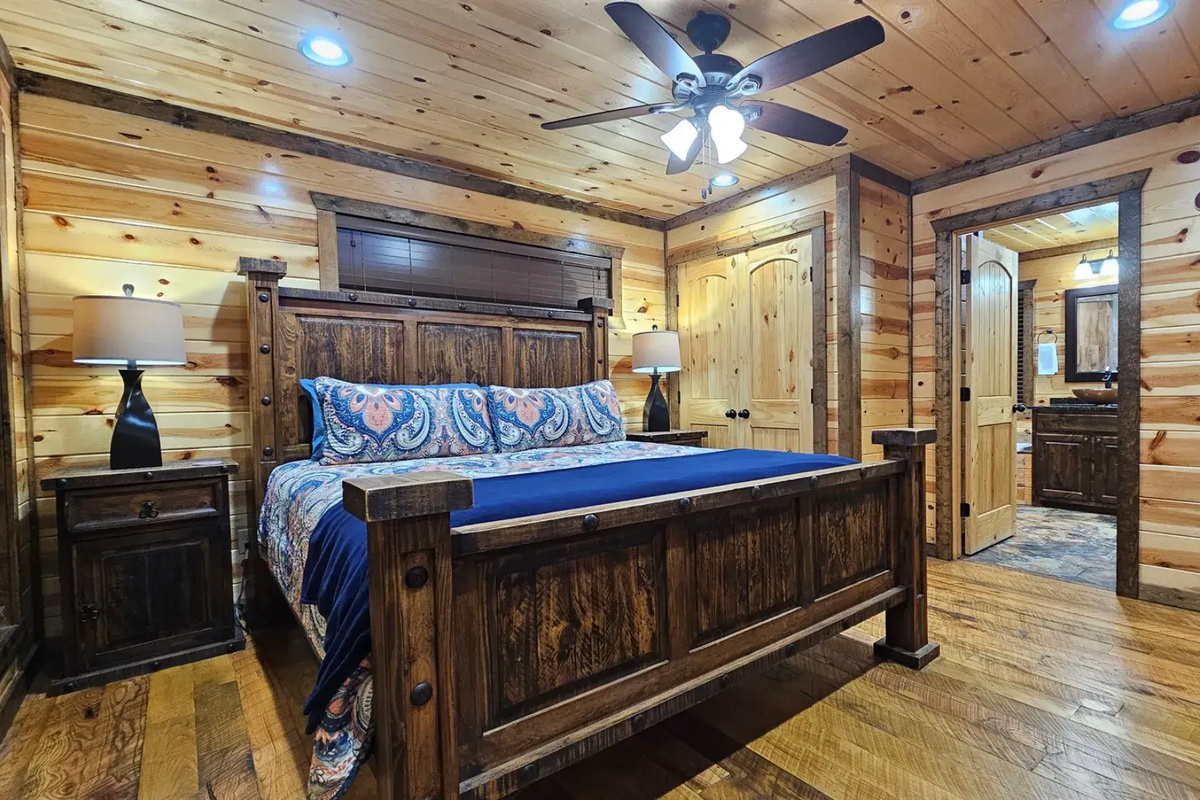 Bedroom 1: Relax in rustic charm with a plush bed and nature views through sunny windows!