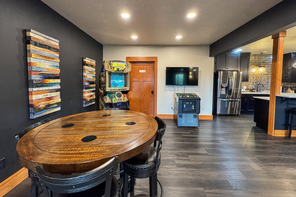 Game area with arcade machines and a gathering table beside the downstairs kitchen.