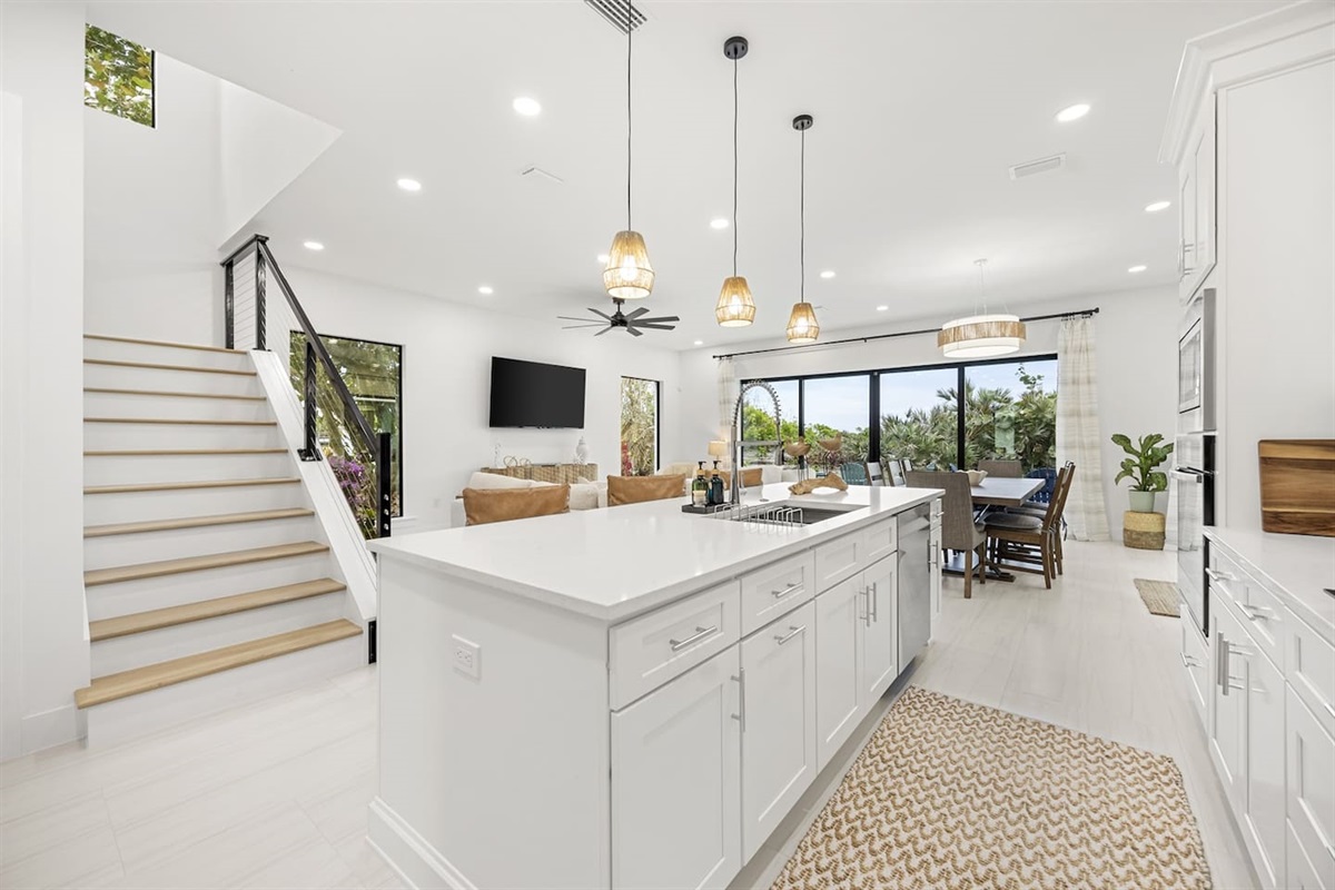 An overview of the kitchen island, looking out to the dining and living room, with a glimpse of the staircase leading upstairs, creating an open and inviting space.