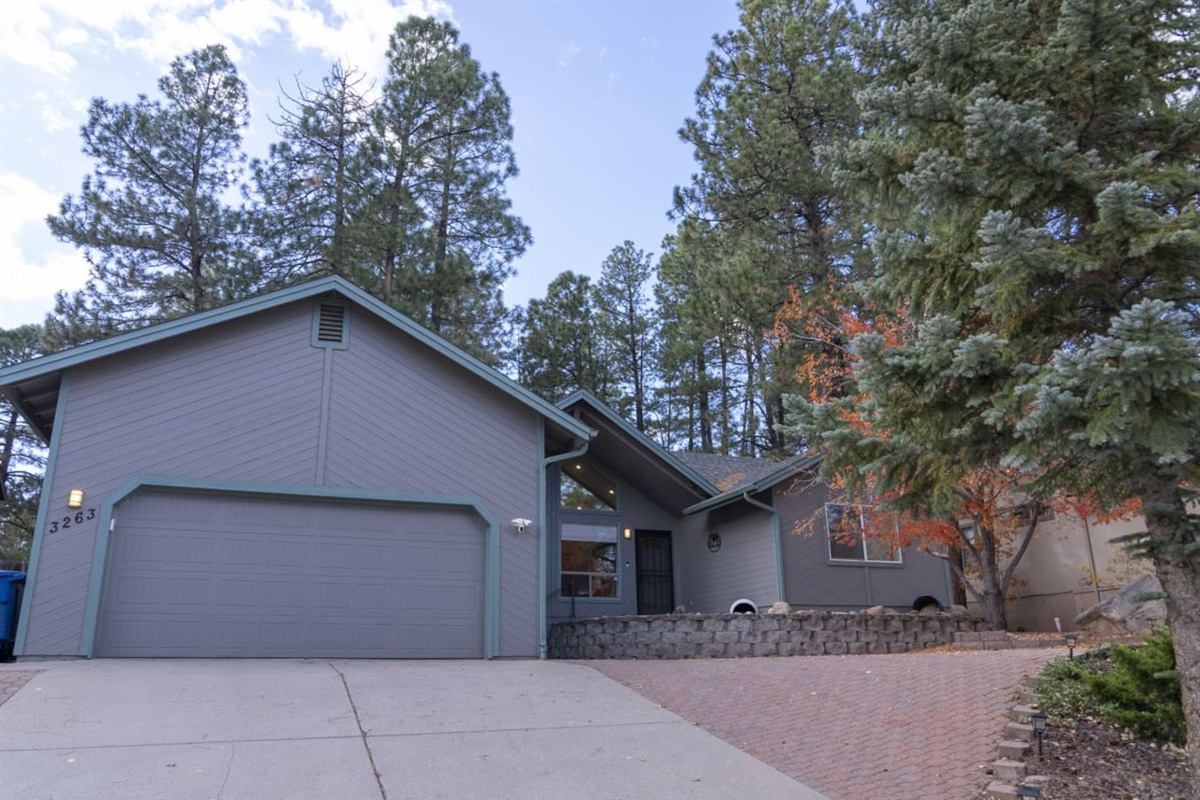 Exterior view with garage access, spacious driveway, and tall trees around the home.