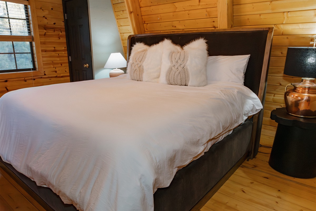 The inviting bedroom at Poppywood Pines features crisp linens with plush faux fur accents for ultimate comfort. This cozy Show Low A-frame offers restful nights surrounded by ponderosa pines, perfect after exploring White Mountains hiking trails and fishin