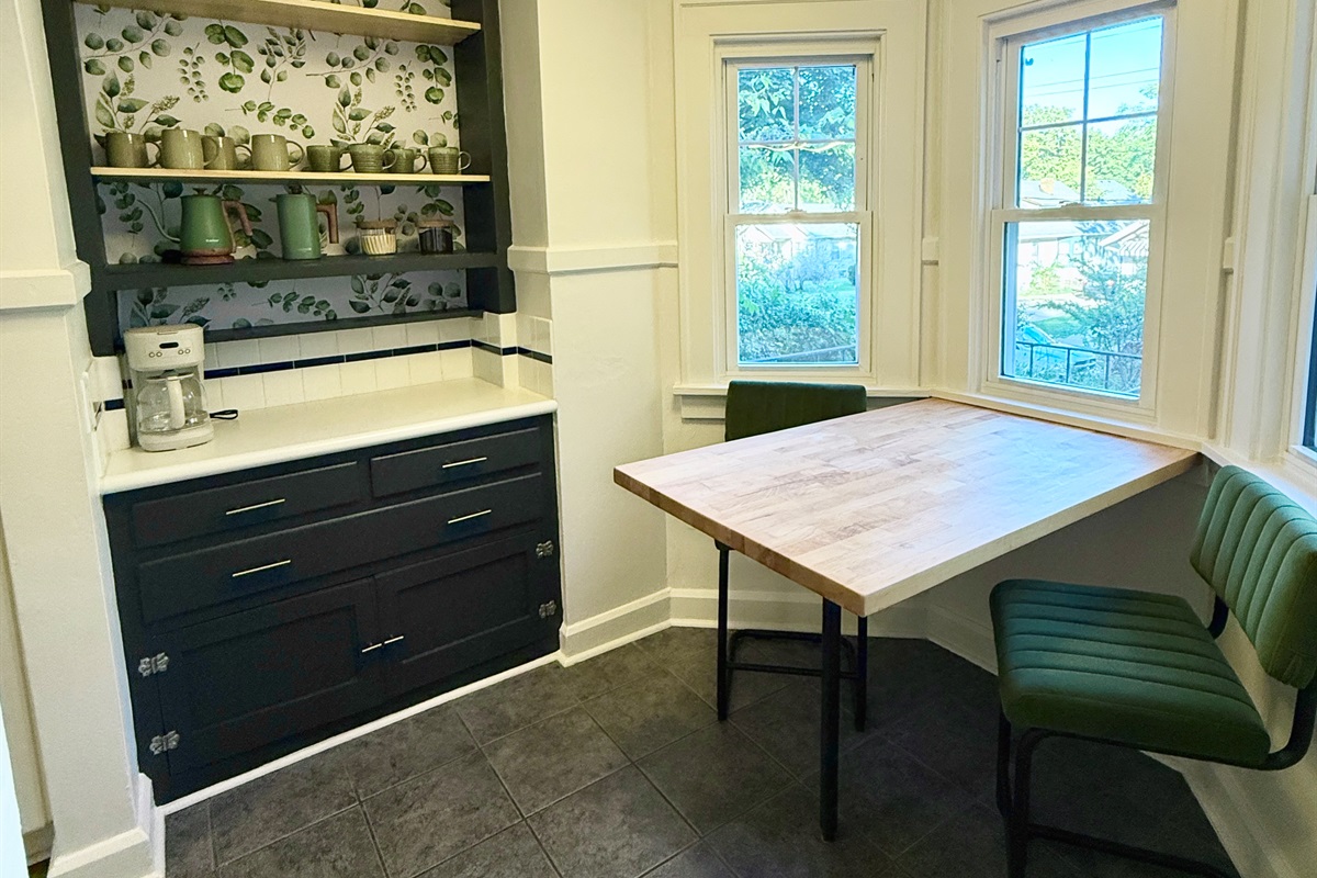 Breakfast nook and coffee station equipped with a coffee maker, electric kettle, french press, and large mugs.