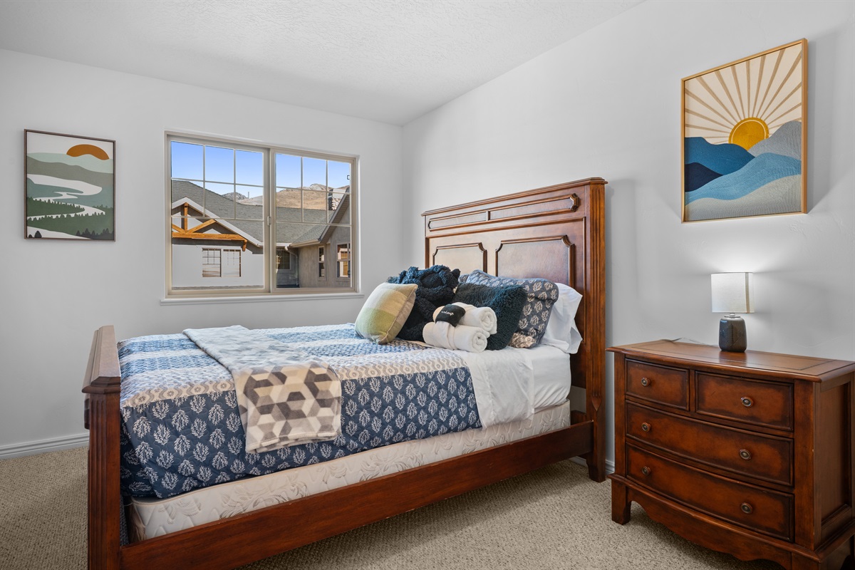 Bright and inviting bedroom with queen bed, warm wood furnishings, and plenty of natural light.