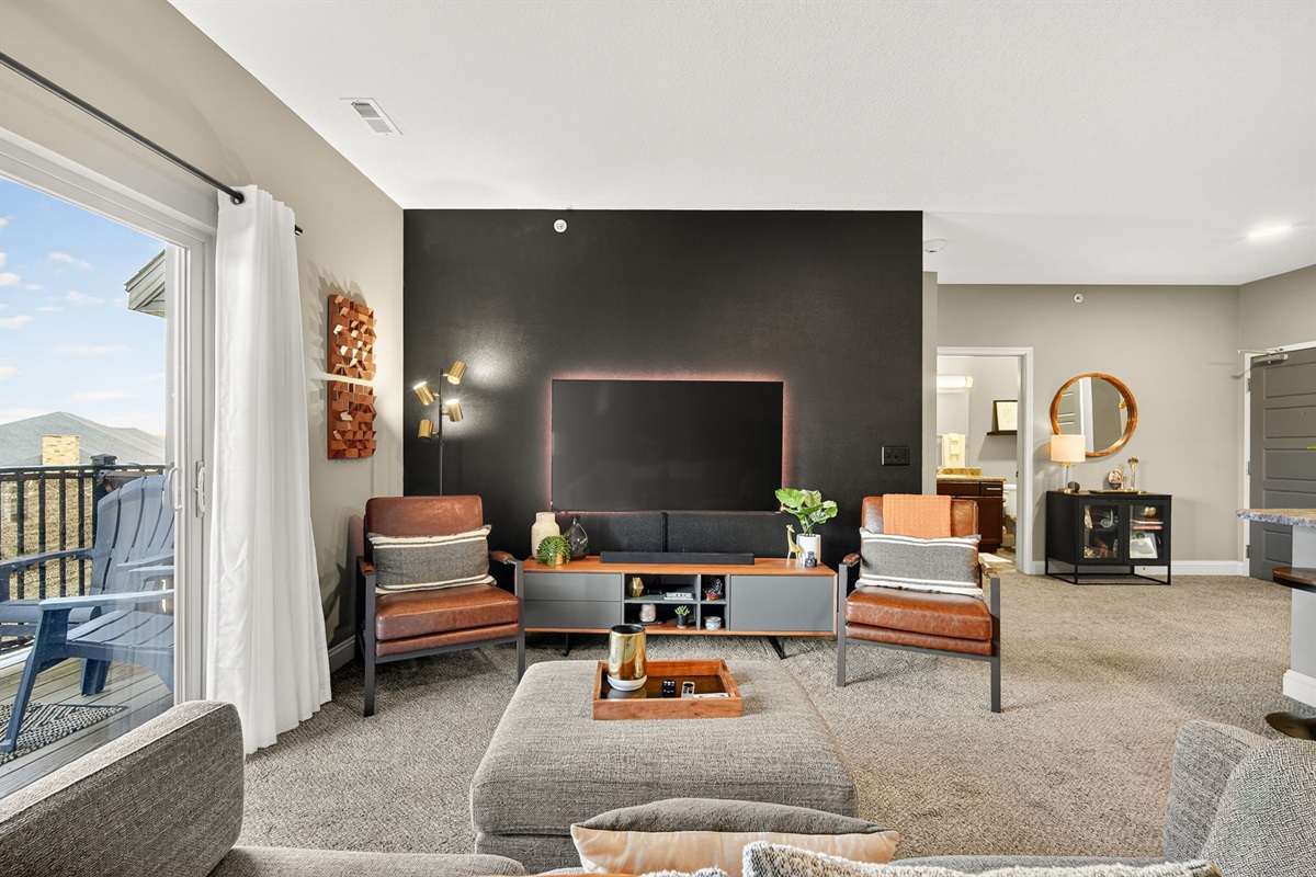 Custom black accent wall with mounted TV creates a bold, modern focal point in the living room. Chic leather chairs, stylish décor, and designer lighting.