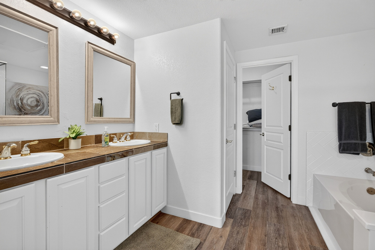 Bathroom vanity with double sinks, bright mirror lighting, cabinet storage, easy access to the nearby shower  and king bedroom 
