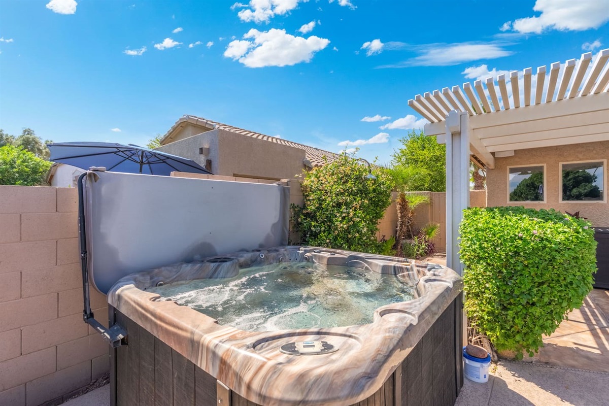 A secluded hot tub nestled in a lush, landscaped corner of the yard — the pergola overhead and greenery all around make it feel like your own private hideaway.