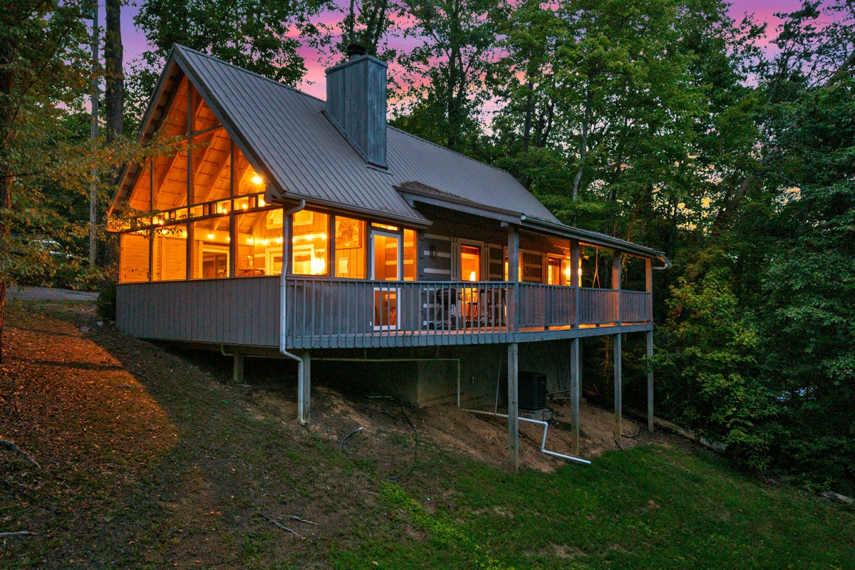Charming Smoky Mountain cabin in Pigeon Forge with glowing windows, a covered porch, and wooded privacy — your perfect Tennessee getaway
