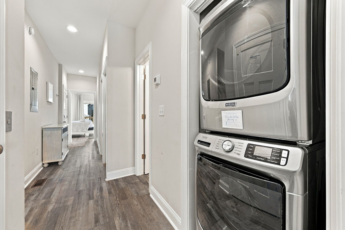 Convenient in-unit laundry closet featuring a modern stacked washer and dryer unit set along a bright hallway with wood-look flooring.
