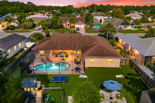 Welcome to your ultimate backyard oasis! This stunning aerial view shows off the fully screened pool, turf yard, putting green, playset, ping-pong table, cornhole, and patio seating. There is endless outdoor entertainment for everyone in your group!
