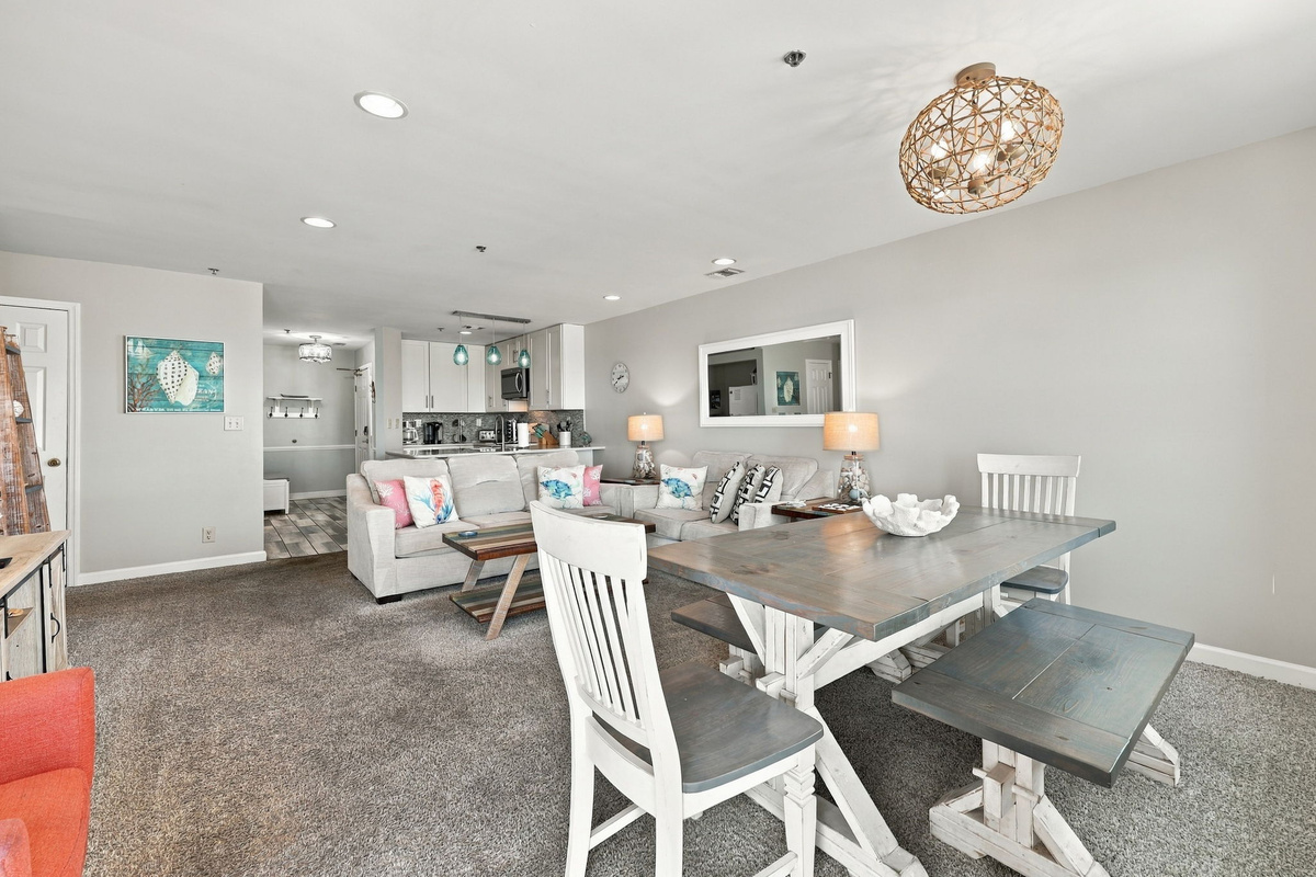 Coastal dining area featuring a rustic wooden table with bench seating, woven pendant light, and open flow into the main living space.   