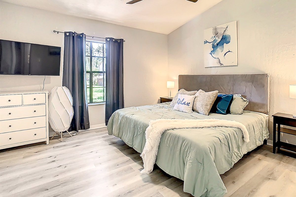 Comfortable bedroom featuring queen bed, large window with natural light, and ceiling fan for guest comfort.