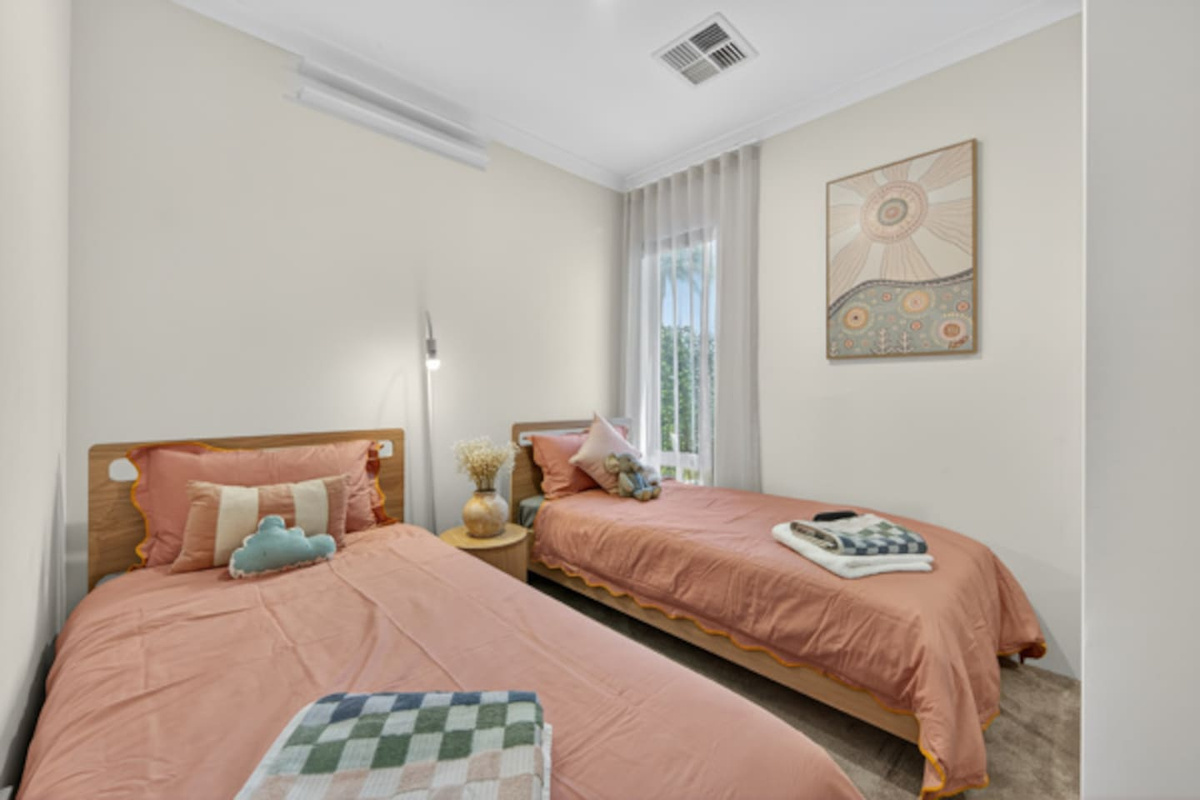 Bright twin room with two single beds in soft peach linen, a bedside reading light, ducted air and fresh towels ready for each guest.