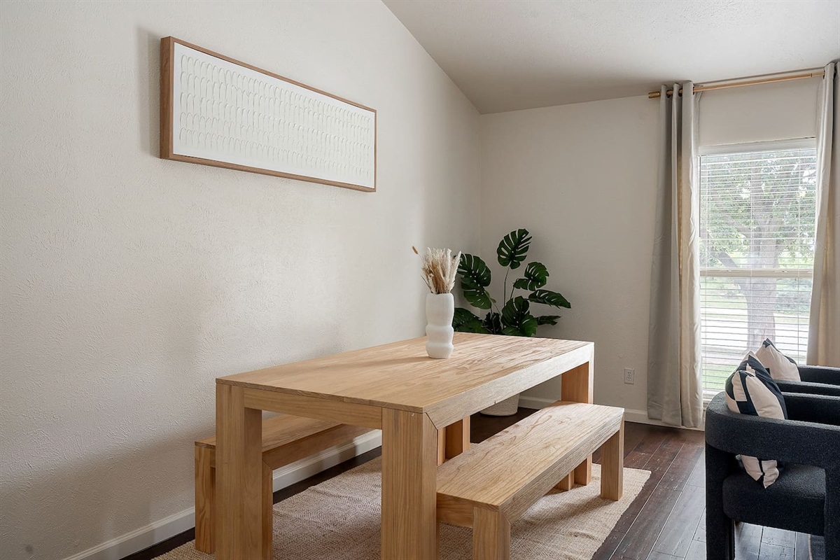 This inviting dining area features a sleek wooden table with matching benches, enhanced by natural light from the large window and tasteful decor.