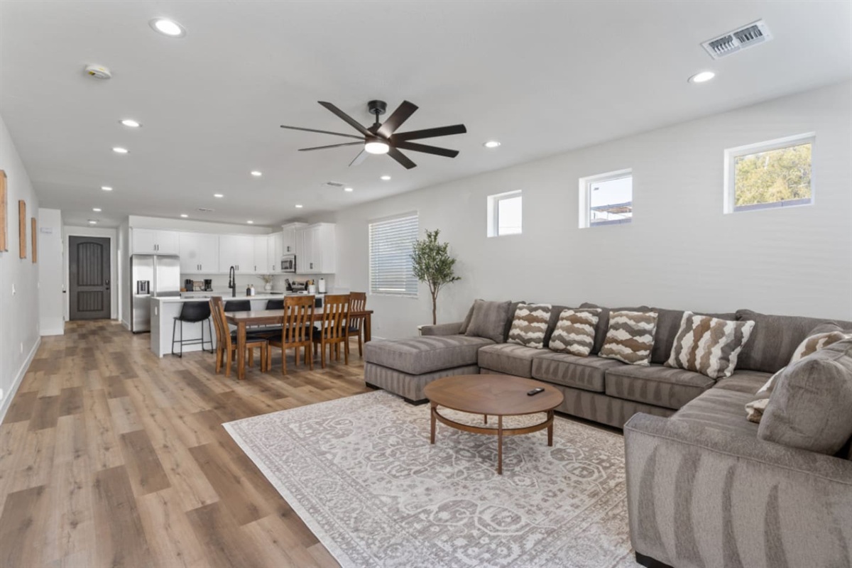 Large living and dining area with a comfortable sectional, ceiling fan, and connected kitchen.