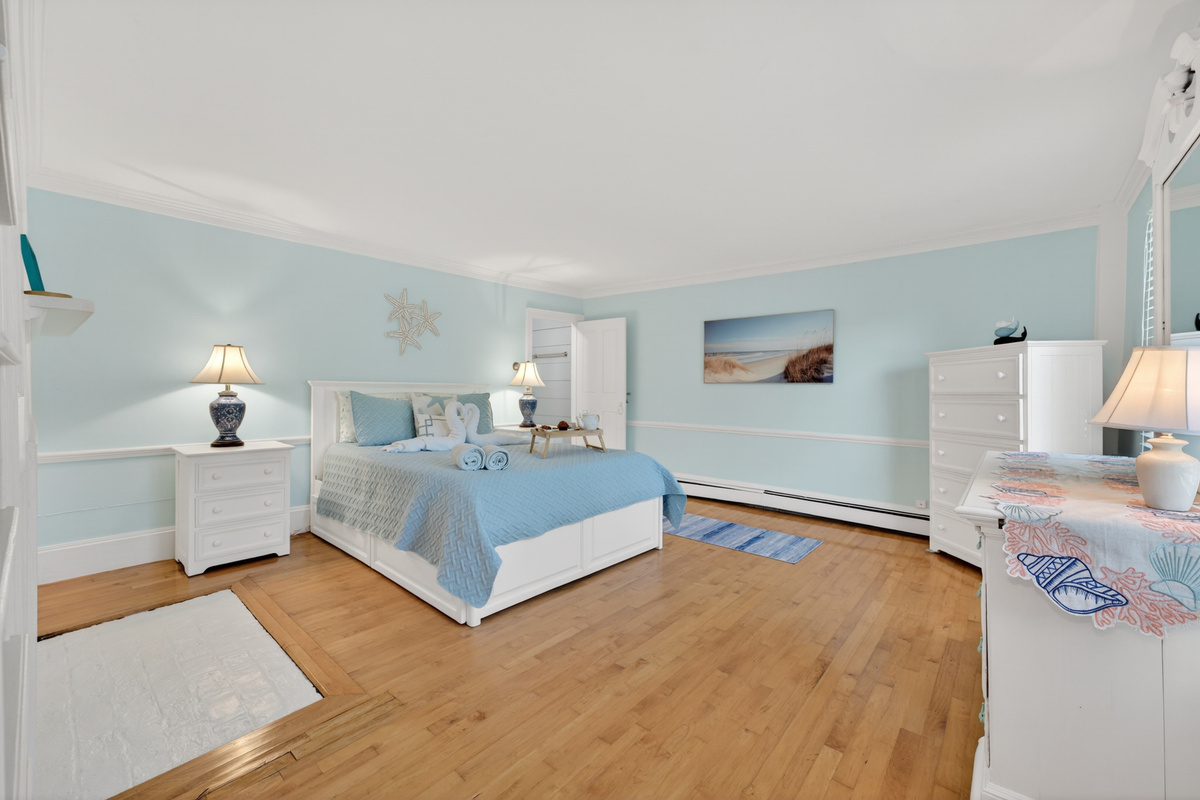 Bright and airy primary suite with a comfortable bed, hardwood floors, and relaxing coastal touches.