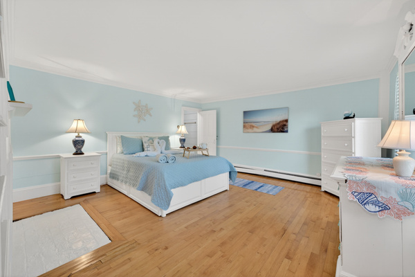 Bright and airy primary suite with a comfortable bed, hardwood floors, and relaxing coastal touches.