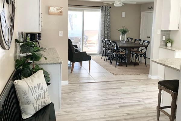 Enjoy the spacious feel of our open-concept home. The view from the entryway reveals a seamless flow from the stylish coffee station to the large farmhouse dining table, all flooded with natural light from the sliding glass doors.