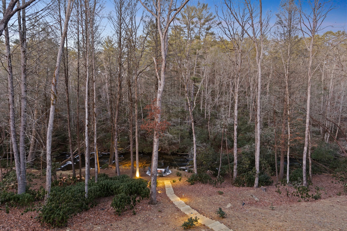 Custom landscape uplighting creates a magical ambiance, guiding your steps with a warm glow as you wander to and from the firepit and the tranquil creek.