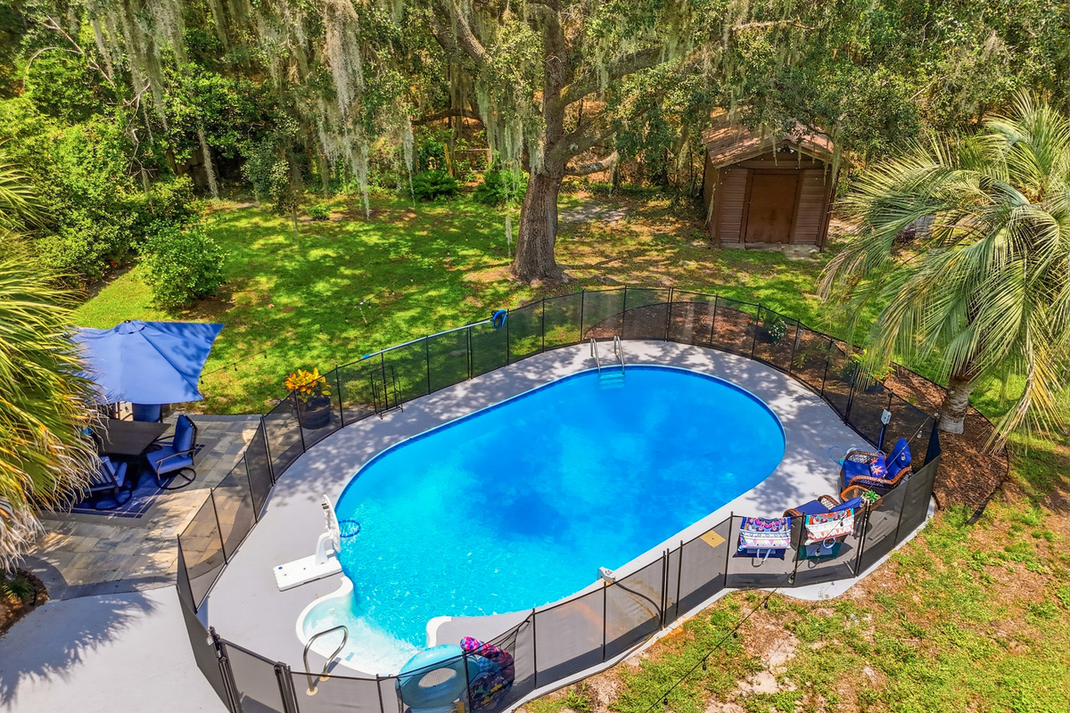 An aerial view highlights the private fenced pool, spacious backyard, mature trees, and peaceful wooded setting.