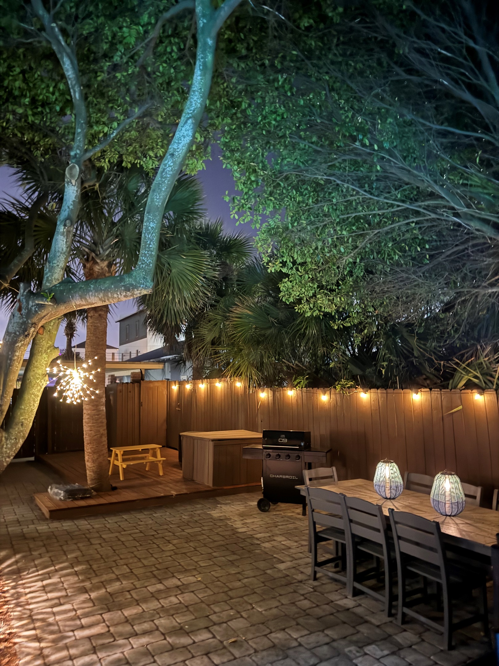 After dark, the backyard comes alive. Brick pavers glow under lanterns, the dining table is set for late-night bites, and the lit pool beckons beyond the gas grill.